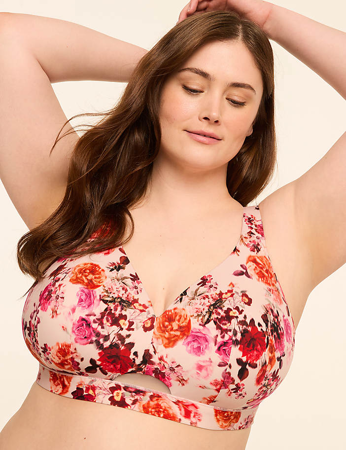 A woman with her arms raised behind her head wears a floral-patterned bra against a plain, light-colored background.