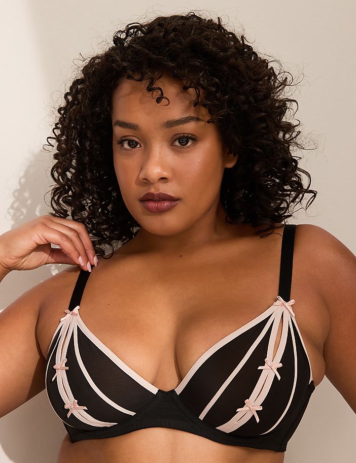 A woman with curly dark hair wears a black and pink bra, with a plain light background.