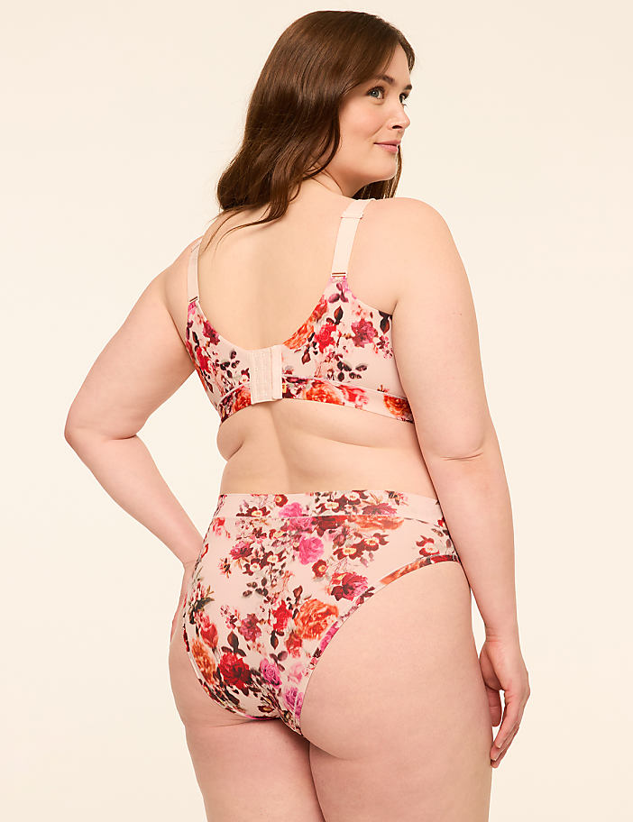 A woman in a floral bra and high-waisted panties stands against a plain, light-colored background.