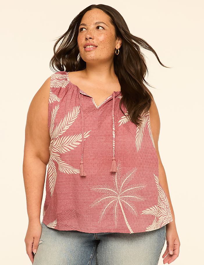 A woman in a red palm-print top and jeans stands against a plain, light-colored background.