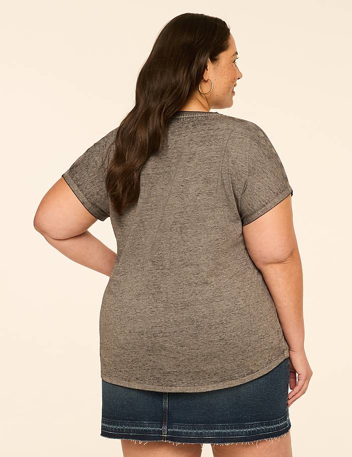 A woman in a grey t-shirt and denim skirt stands against a plain, light-colored background.