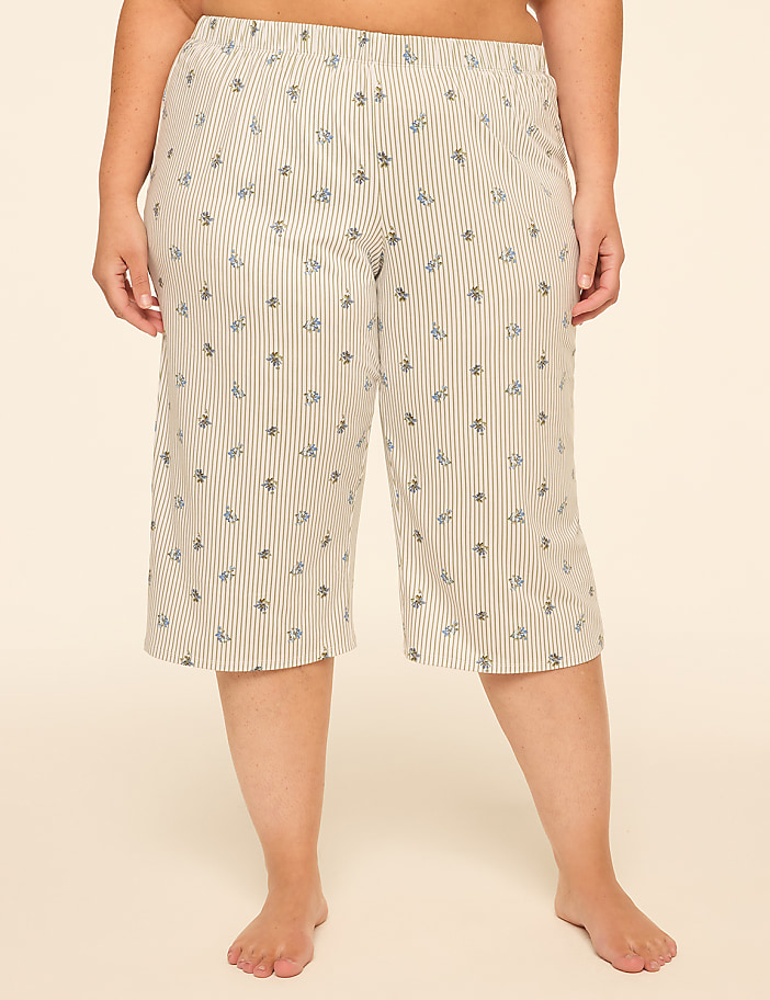 A person stands in cropped, striped pajama pants with a floral pattern against a plain, light-colored background.