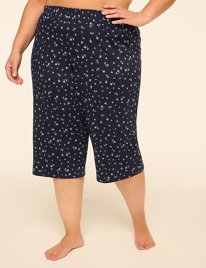 A person stands in cropped, floral-patterned pants against a plain, light-colored background.