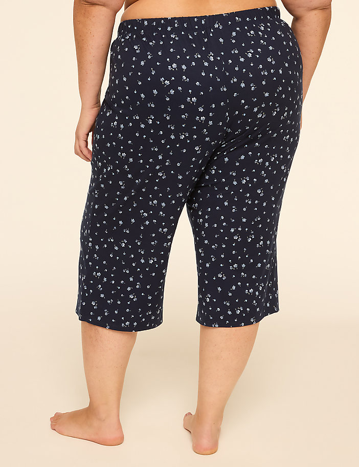 A person's back is shown from the waist down, wearing navy blue capri pants with a small white floral pattern, against a plain beige background.