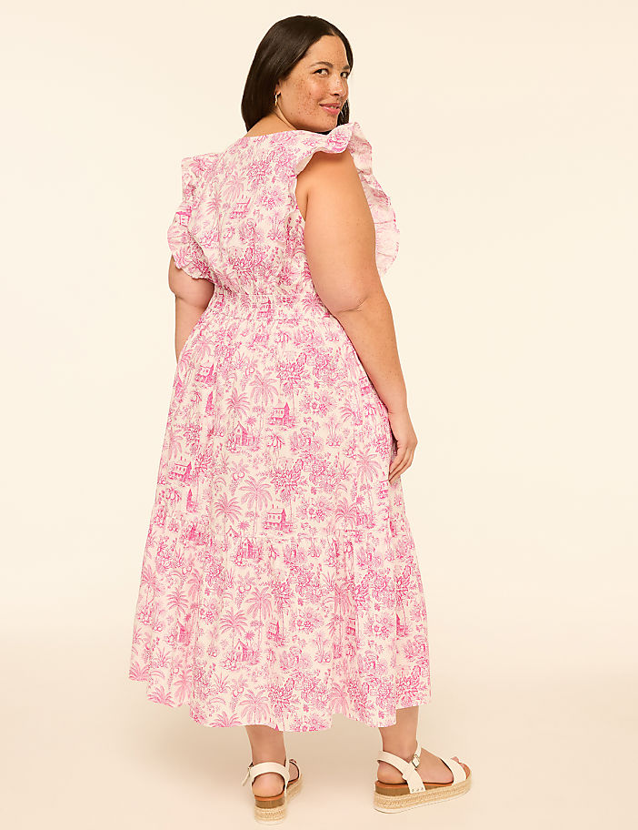 A woman in a pink floral dress stands against a plain, light-colored background.