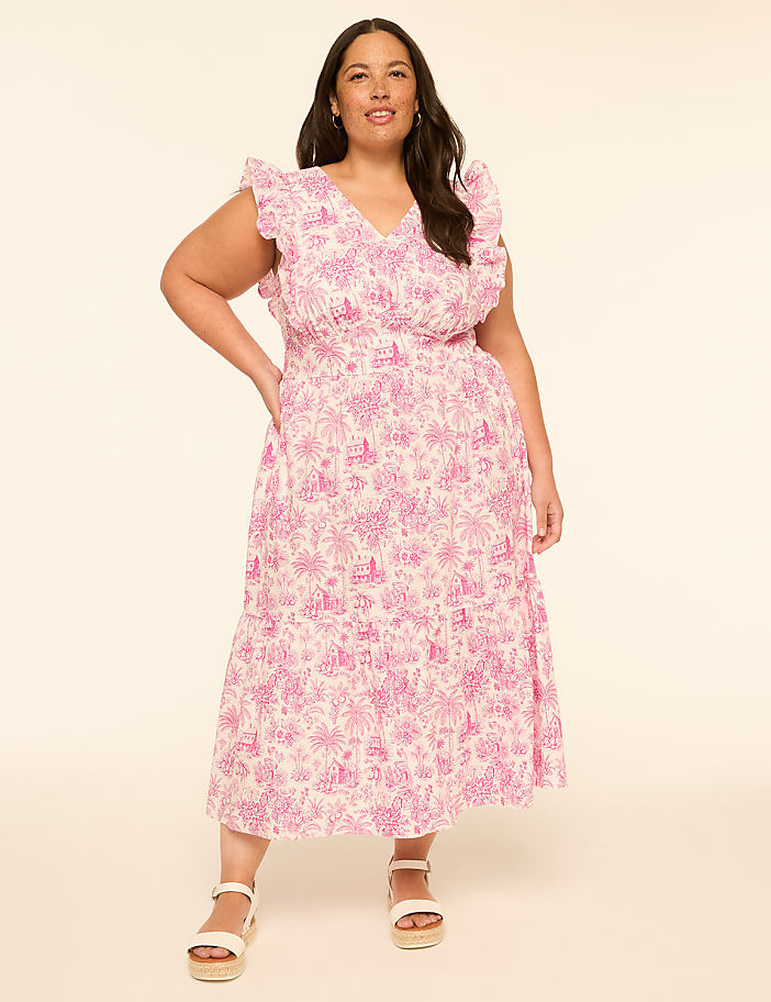 A woman in a pink floral dress stands against a plain, light-colored background.