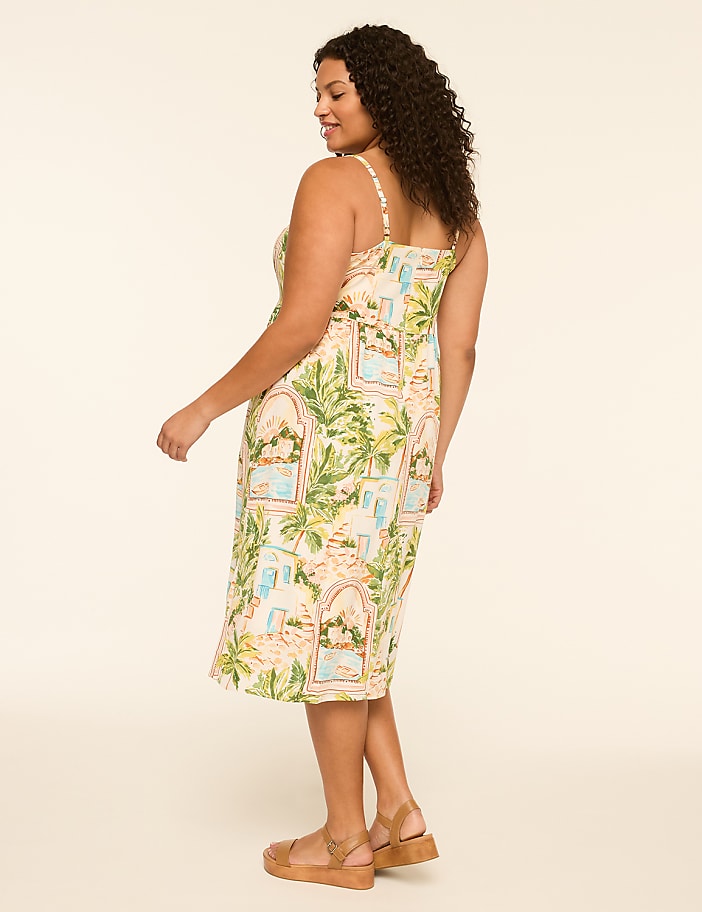 A woman in a tropical-print dress and sandals stands against a plain, light-colored background.