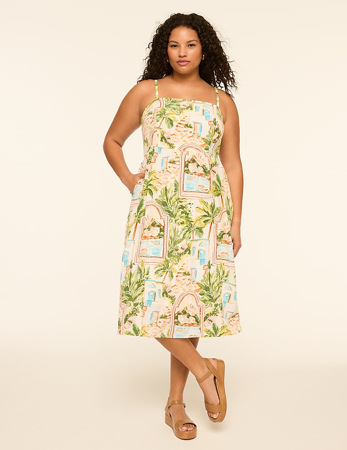 A woman in a patterned dress stands against a plain, light-colored background.