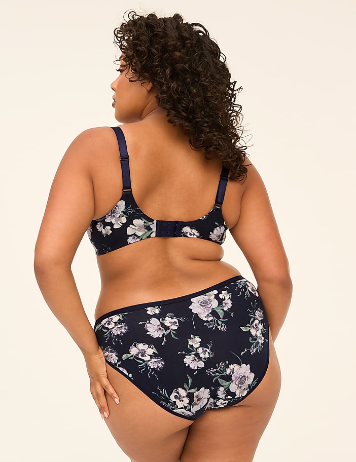 A woman in a floral bra and matching underwear stands against a plain, light-colored background.