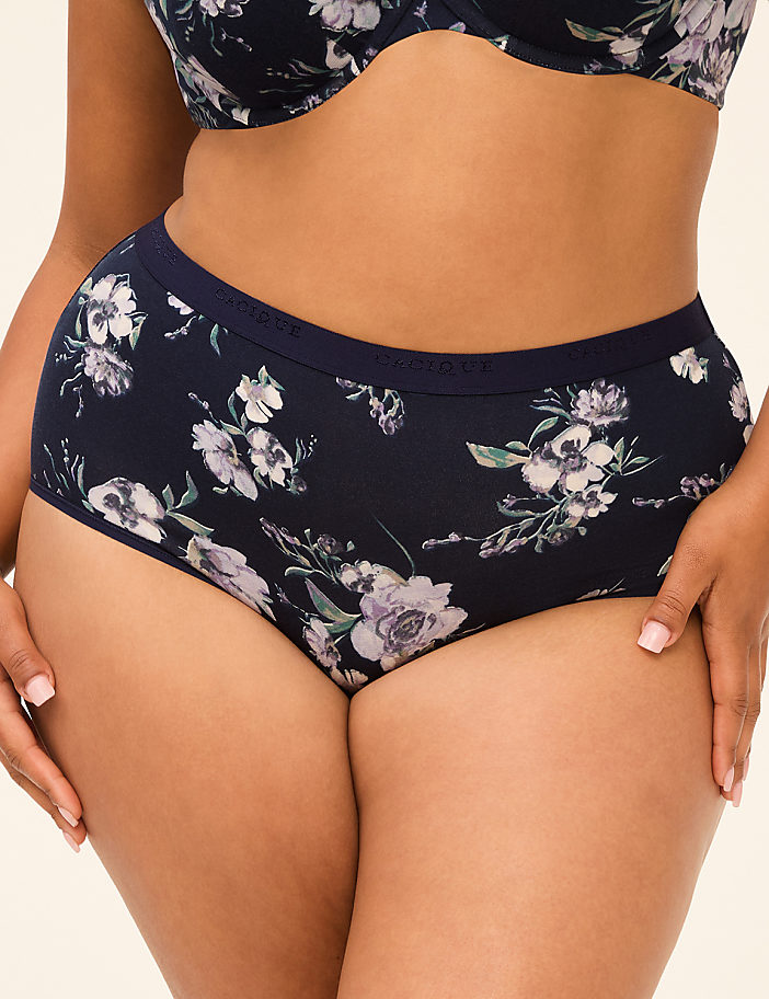 A woman in floral patterned underwear stands against a plain, light-colored background.
