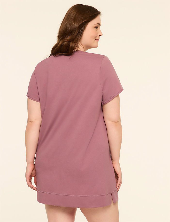 A woman in a mauve t-shirt dress stands against a plain, light-colored background.