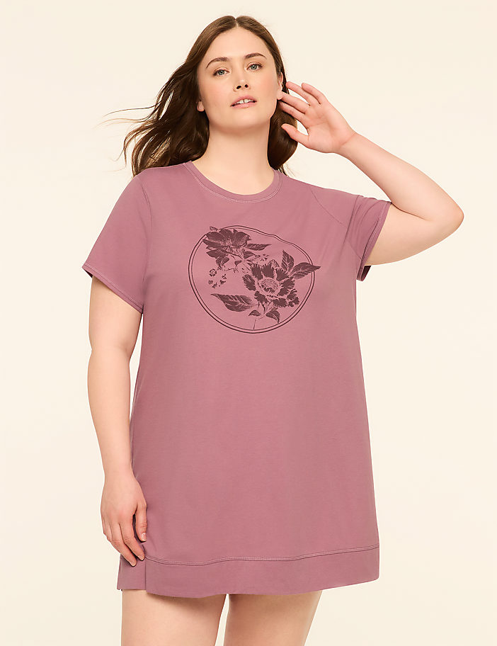 A woman in a mauve t-shirt with a floral graphic stands against a plain, light background.