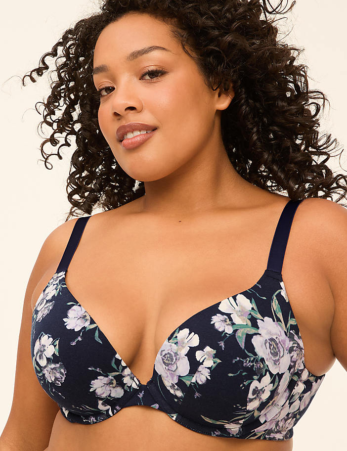 A woman with curly dark hair wears a navy blue floral bra in the foreground, against a plain, light-colored background.