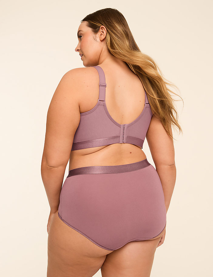 A woman in a mauve bra and high-waisted underwear stands against a plain, light-colored background.