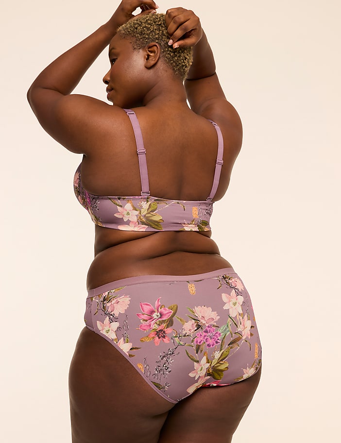 A woman in floral lingerie stands against a plain, light-colored background.