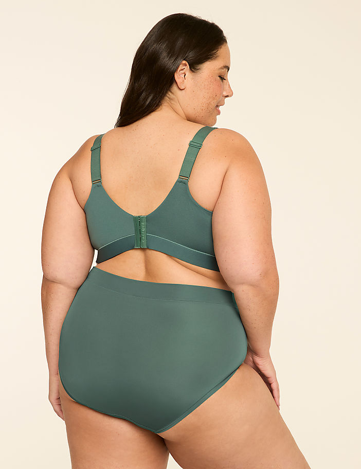 A woman in a green bra and underwear stands against a plain, light-colored background.
