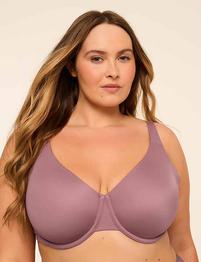 A woman with long blonde hair wears a mauve bra against a plain beige background.