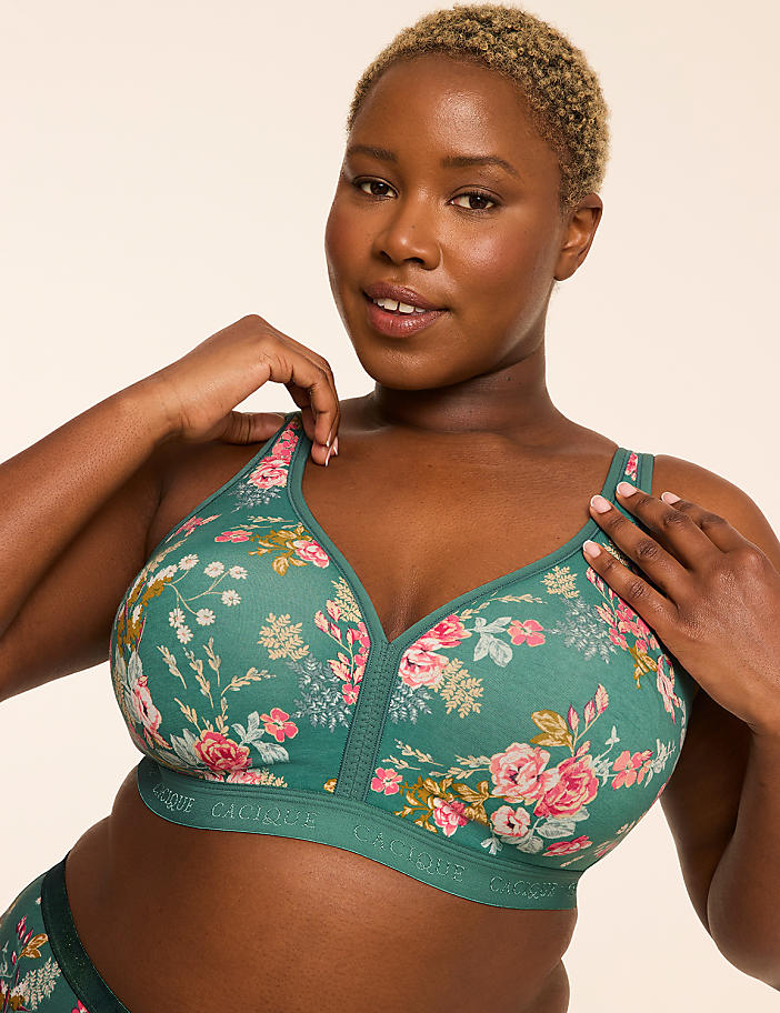 A woman with short blonde hair and dark skin wears a floral green bra, with a plain beige background.