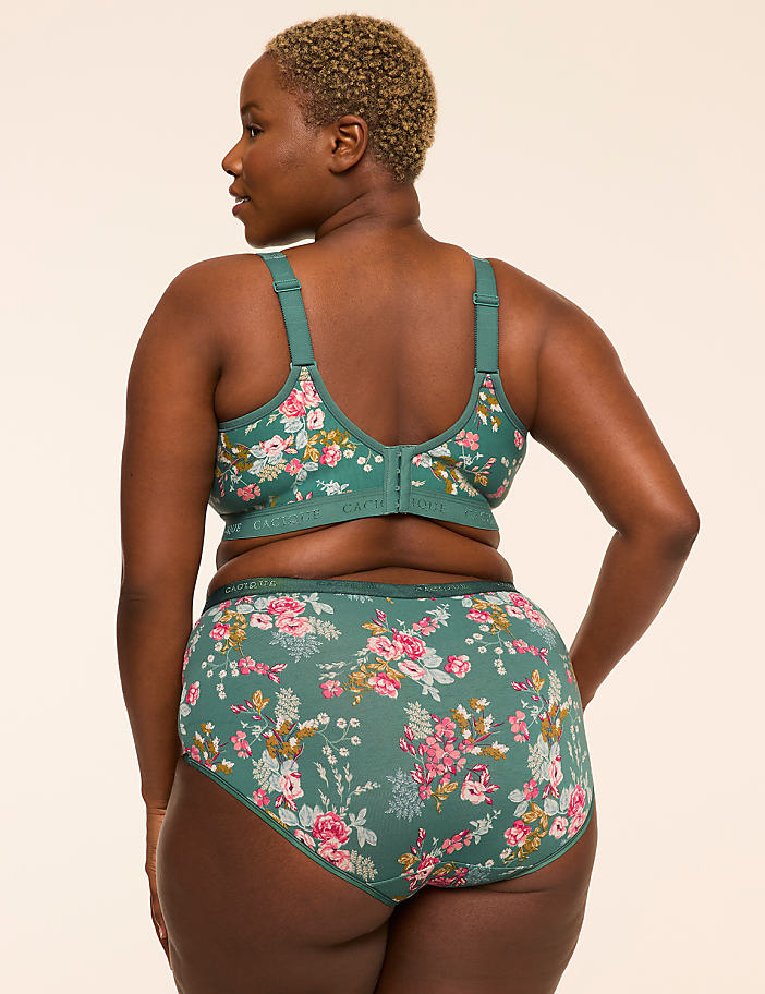 A woman in a floral bra and underwear stands against a plain, light-colored background.