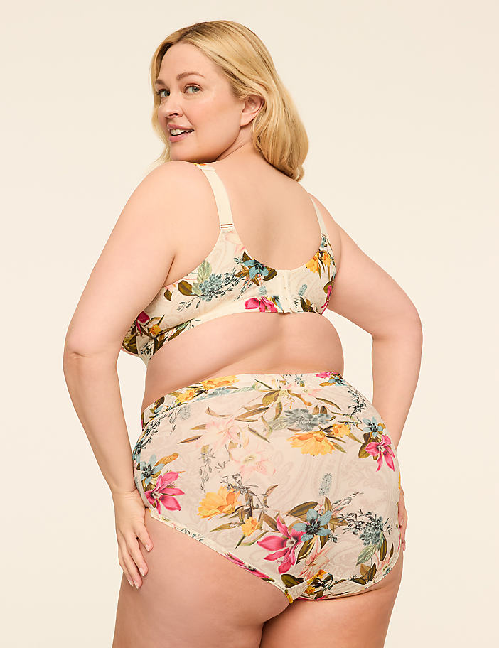 A woman in a floral bra and underwear turns to smile over her shoulder against a plain, light background.