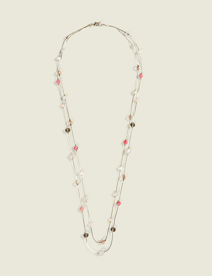 A delicate, multi-strand necklace with pink and clear beads is displayed against a plain, light beige background.