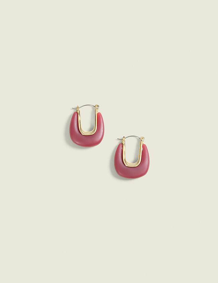 A pair of matte pink U-shaped earrings with gold accents rests on a pale yellow background.