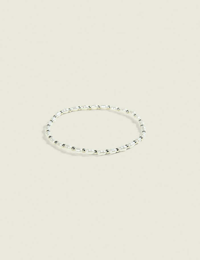 A delicate pearl and silver bead bracelet rests on a soft, pale background.