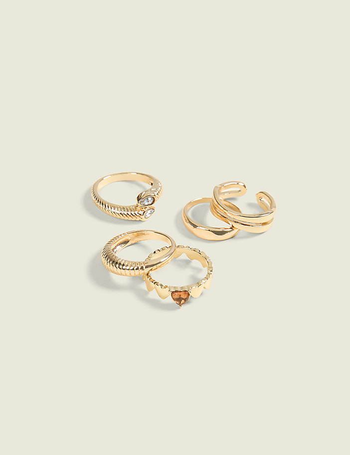 A collection of gold rings, some adorned with stones and intricate designs, are arranged on a pale, textured surface.
