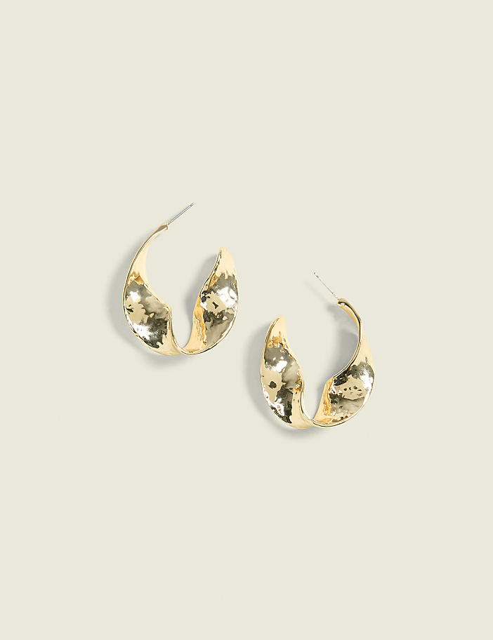 A pair of textured gold hoop earrings rests on a light beige background.