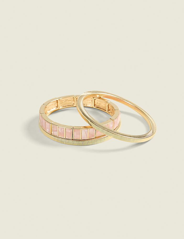 Two gold bracelets, one with pink square stones and the other with a feather design, rest on a pale green background.