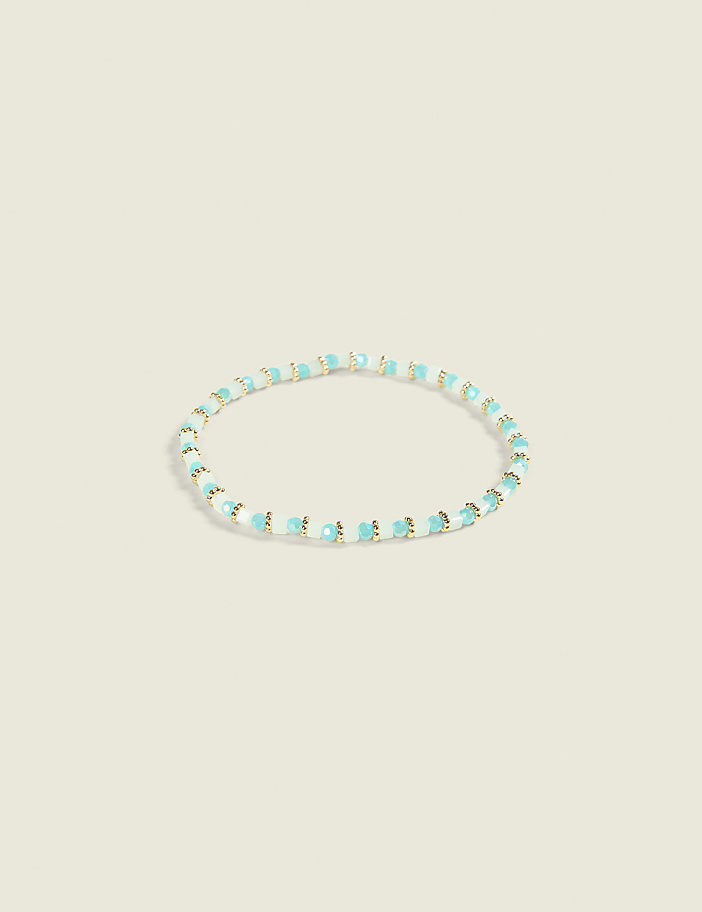 A delicate bracelet with small, light blue and white beads is centered against a soft, pale yellow background.