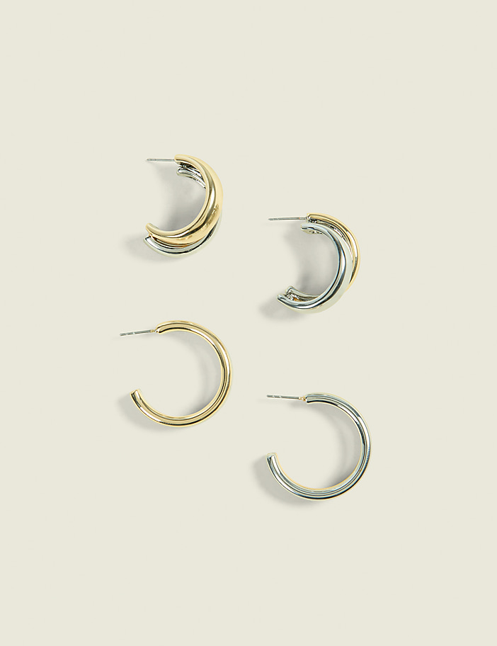 Four hoop earrings, two gold and two silver, are arranged on a plain, light-colored background.