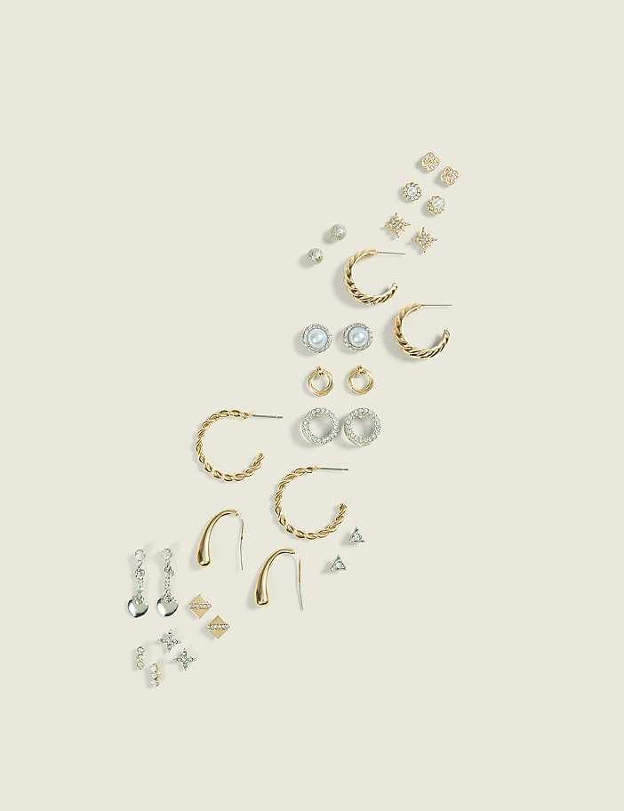 A collection of assorted earrings, including studs and hoops, are arranged diagonally on a plain, light-colored background.