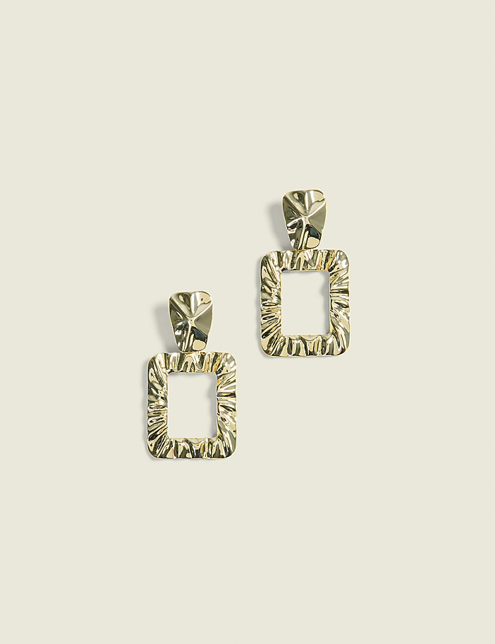 Two gold square-shaped earrings with textured surfaces hang against a plain, light-colored background.
