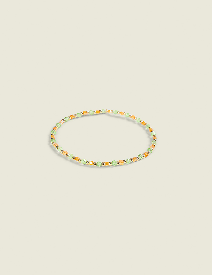 A delicate bracelet with small green and orange beads rests on a plain, light-colored background.