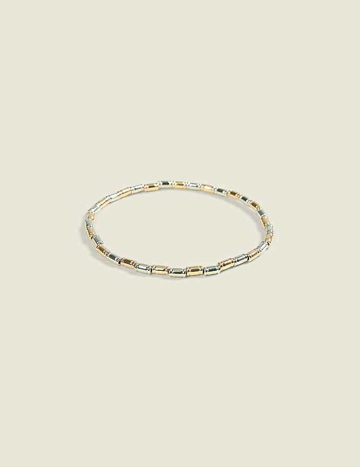 A delicate bracelet with alternating gold and silver rectangular beads rests on a soft, pale background.