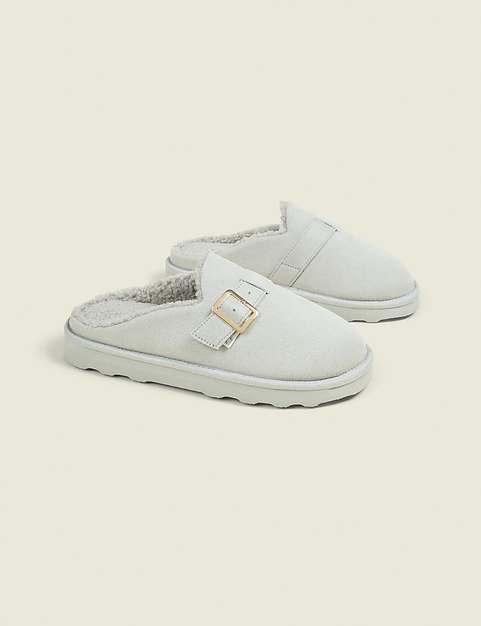 A pair of light gray, fur-lined mule slippers with gold buckles rest on a plain, light beige background.