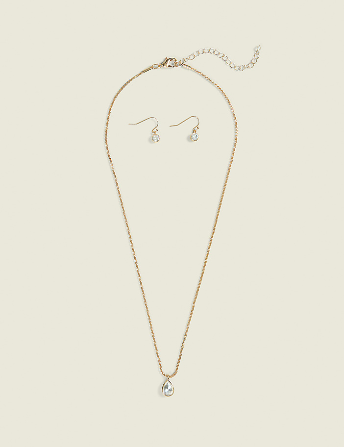 A delicate gold necklace with a teardrop pendant and matching earrings rest on a plain, light beige background.