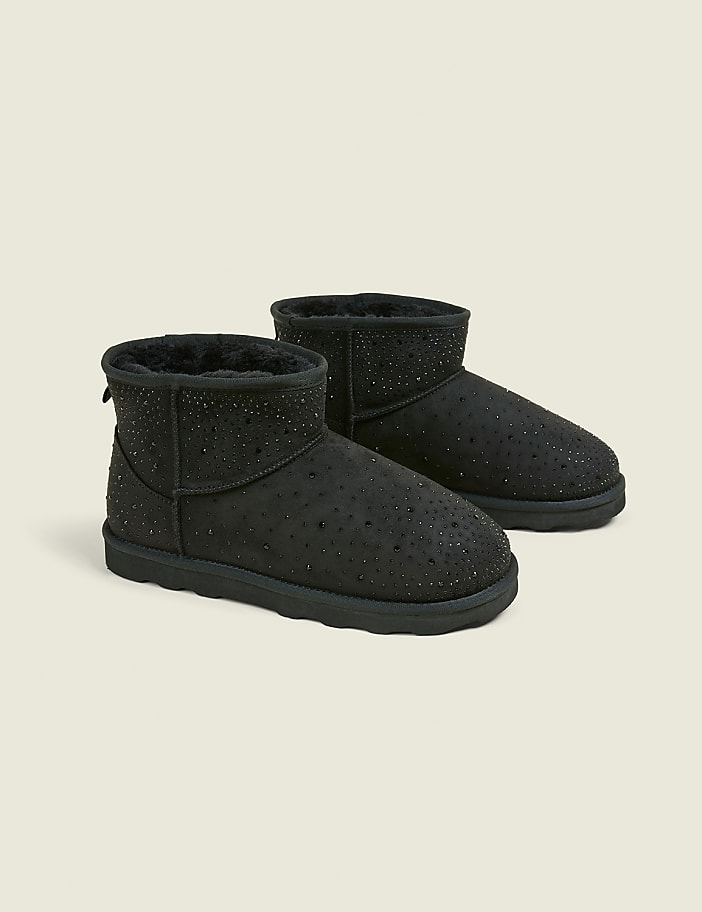 A pair of black, sparkly ankle boots with fluffy lining are displayed against a plain, light gray background.