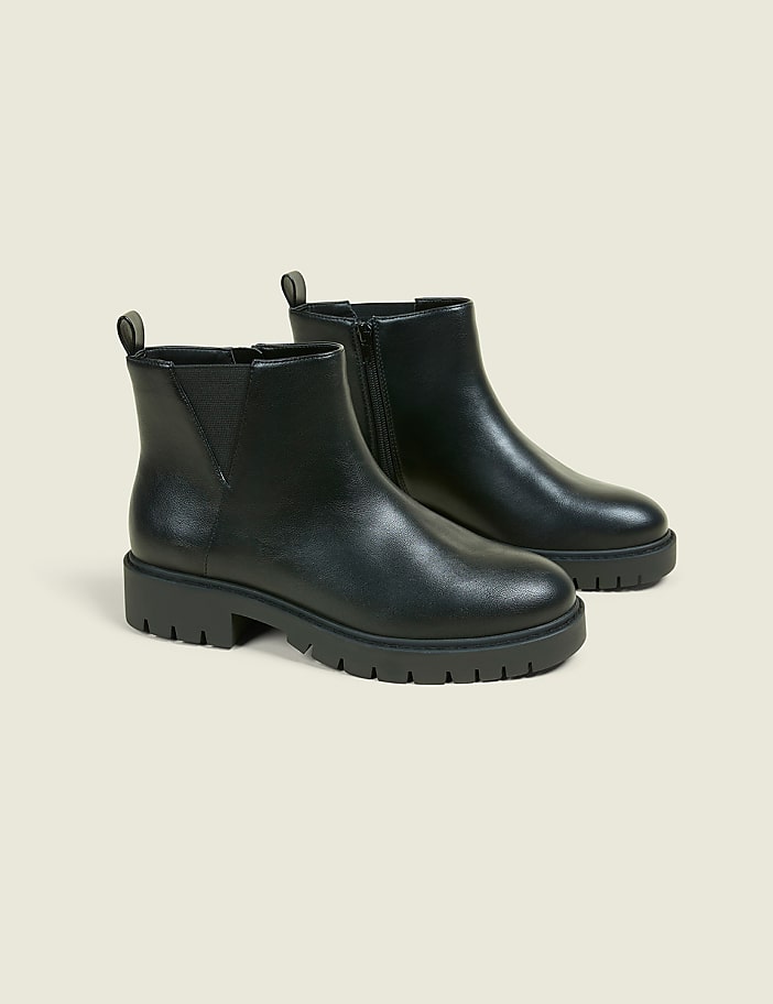 A pair of black Chelsea boots with thick soles are displayed against a plain, light-colored background.