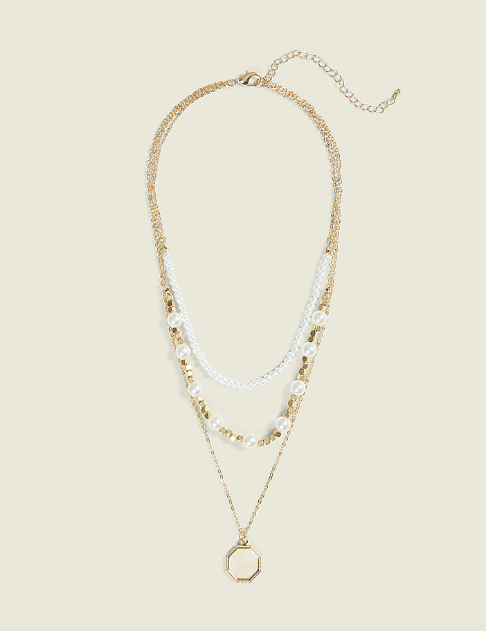 A layered gold necklace with pearls and a locket pendant rests against a plain, light-colored background.