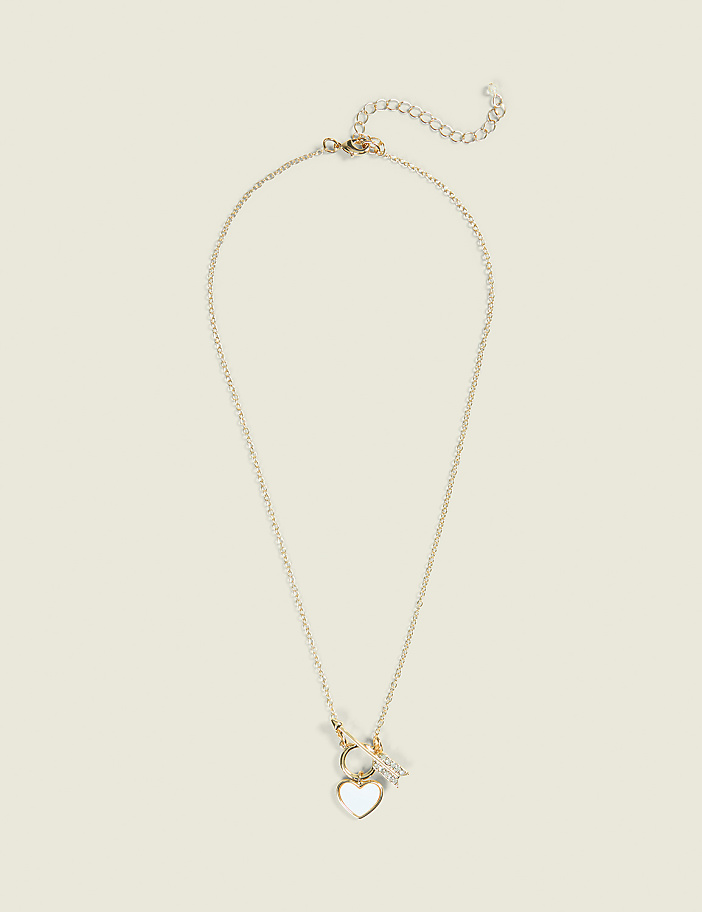 A delicate gold necklace with a heart-shaped pendant hangs against a plain, light-colored background.