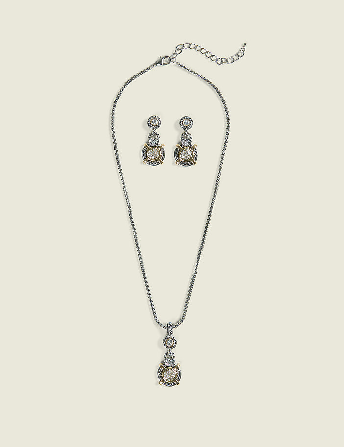 A silver necklace with a pendant and matching earrings, adorned with clear stones and gold accents, are displayed against a pale, textured background.