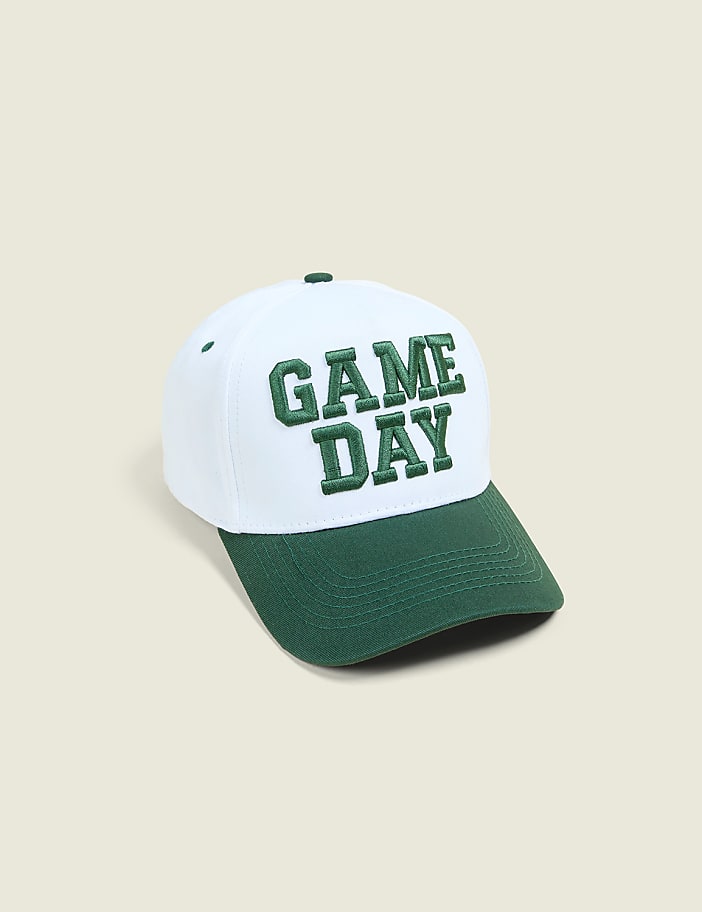 A white baseball cap with green "GAME DAY" lettering sits on a plain, light-colored background.
