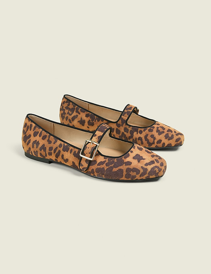 A pair of leopard-print Mary Jane flats with black trim and gold buckles rests on a plain, light beige background.