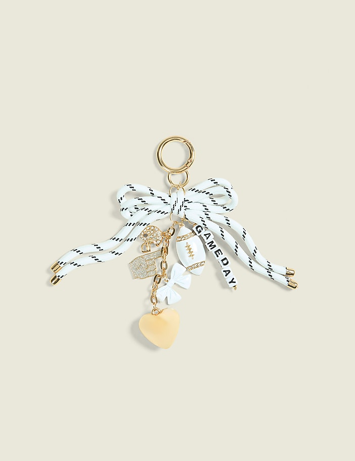 A white and black striped ribbon bow with various charms, including a football, heart, and dice, hangs against a plain, light-colored background.