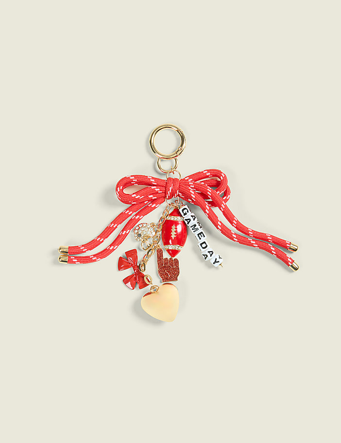 A red bow with various charms, including a football and a heart, hangs against a plain, light-colored background.