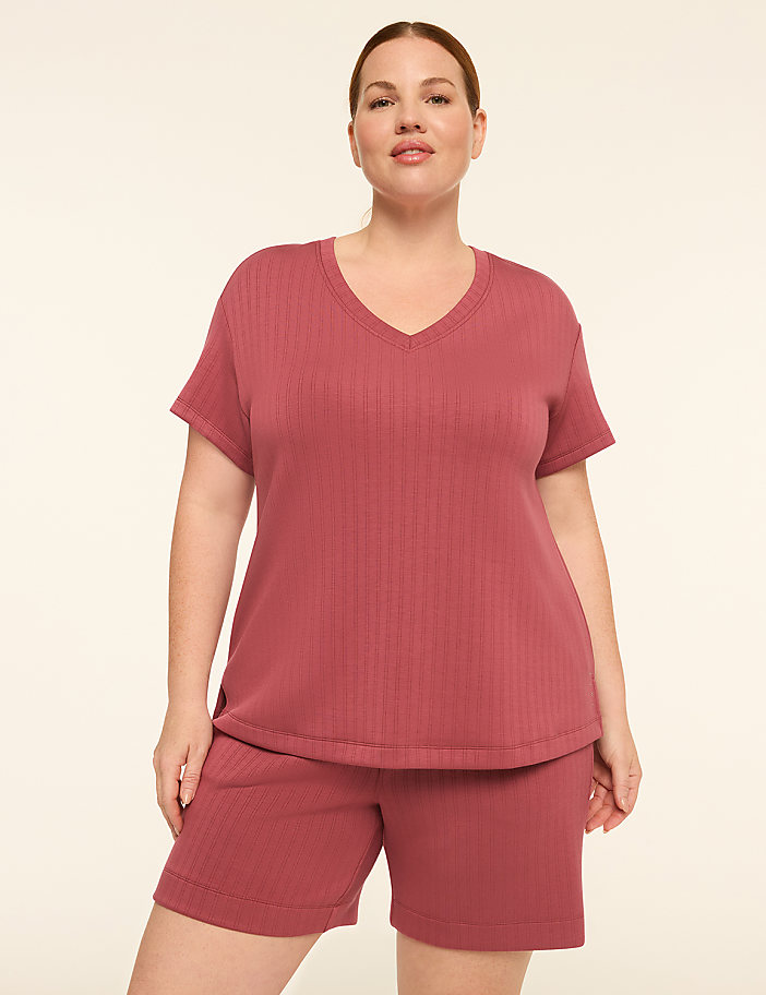 A woman in a rose-colored ribbed pajama set stands against a plain, light-colored background.