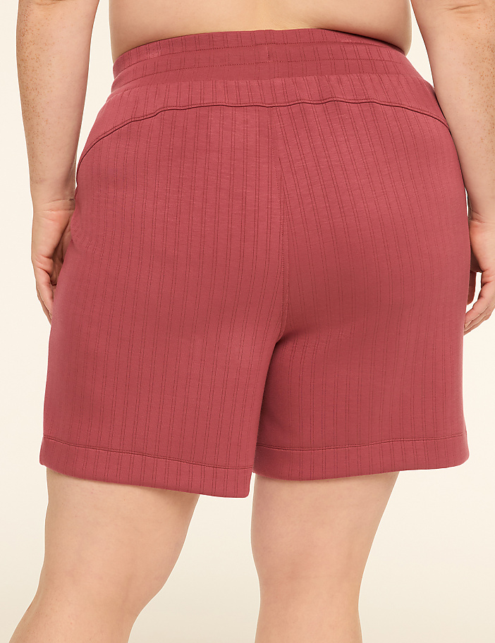 A person wearing ribbed maroon shorts stands against a plain, light-colored background.