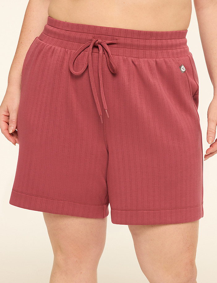 A person wearing rose-colored ribbed shorts with a drawstring stands against a plain, light-colored background.